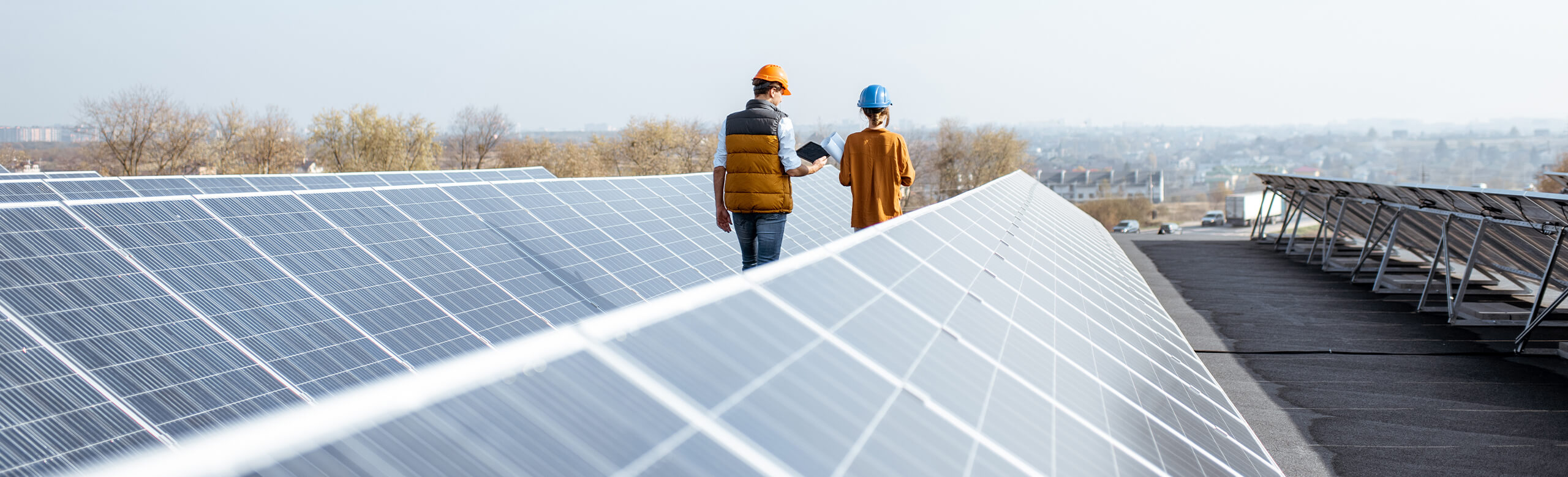 Construction – Solutions de toiture solaire et toit plat pour bâtiments Deux professionnels casqués inspectent des panneaux solaires sur un toit plat; texte « Construction »